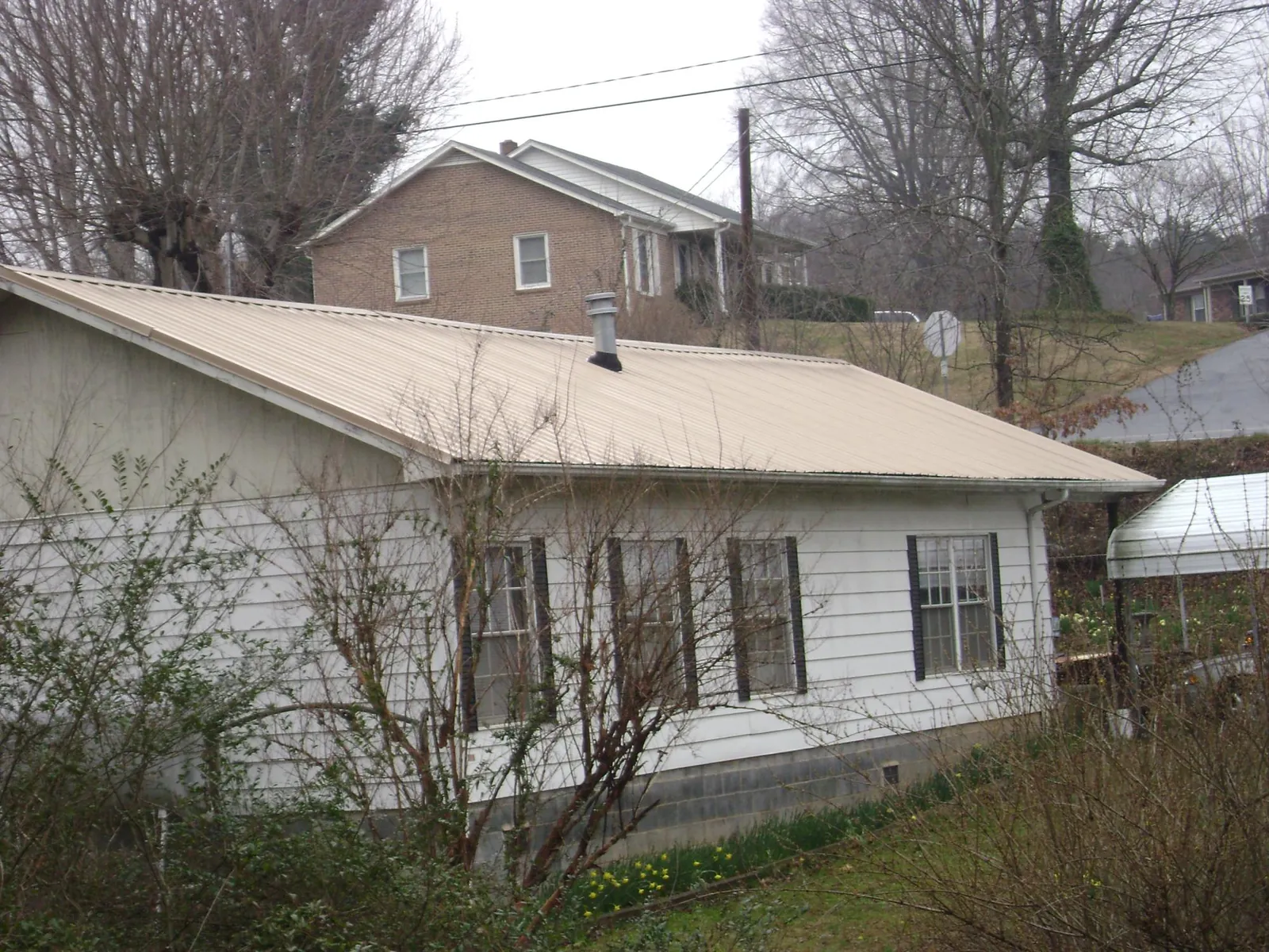 Tan metal roof on a white sided house set into a hillside — Commercial Roofing by Roofing Brothers in Canton